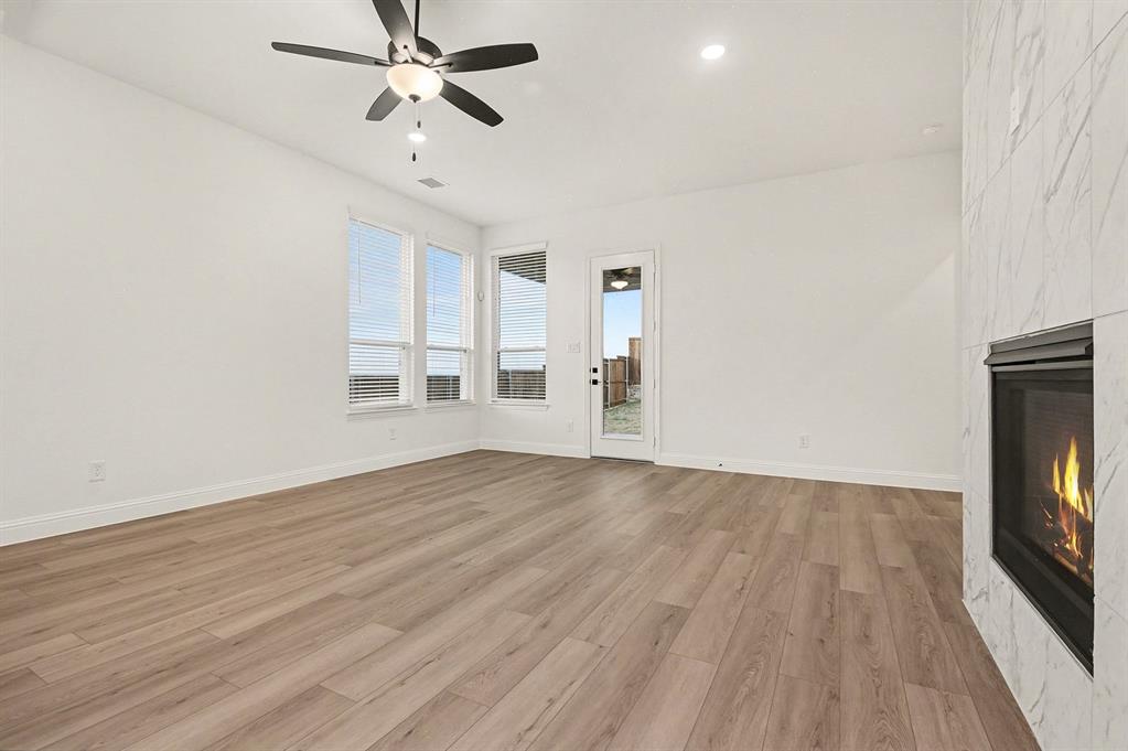 Living area featuring wood-finish flooring, a fireplace with stone-style tile surround, ceiling fan, and large windows