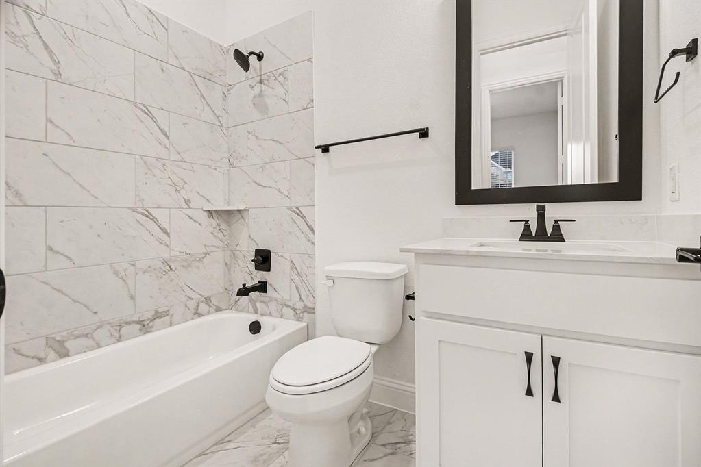 Bathroom featuring a tub-shower combination with floor-to-ceiling stone-look wall tile, white vanity cabinet with a stone countertop, matte black plumbing fixtures, and a framed mirror
