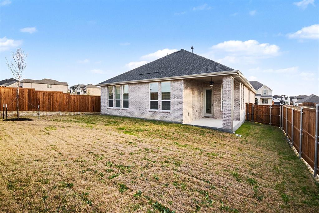 Light brick exterior with a covered rear patio, asphalt shingle roof, and wood privacy fencing