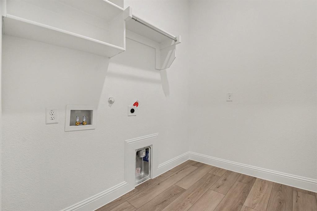 Utility space featuring wood-finish flooring, built-in upper shelving, integrated hanging rod, and recessed plumbing connections
