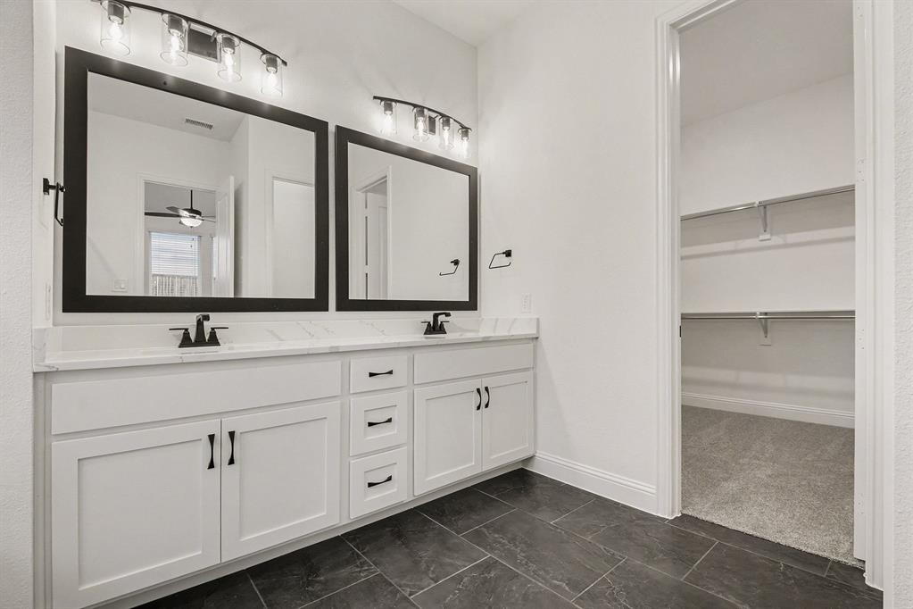 Dual-sink vanity featuring white cabinetry, stone-finish countertops, matte black fixtures, and framed mirrors with overhead vanity lighting, complemented by dark tiled flooring