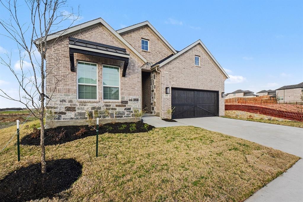 Single-story exterior featuring a brick and stone facade, contrasting dark-toned garage door, metal awning detail, and a concrete driveway Single-story exterior featuring a brick and stone facade, contrasting dark-toned garage door, metal awning detail, and a concrete driveway