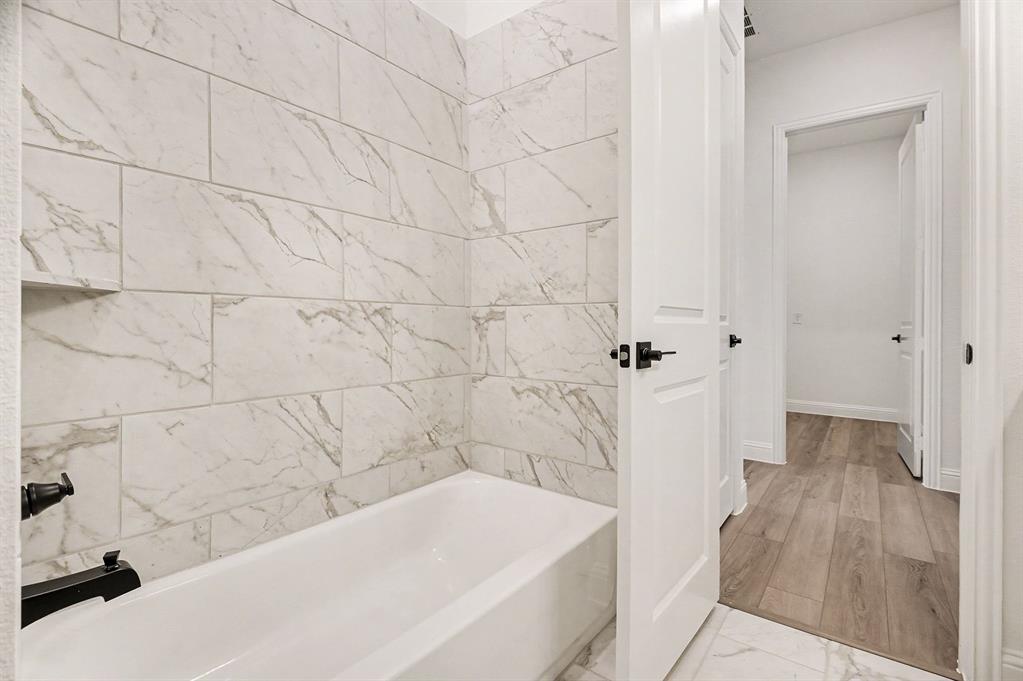 Full-height shower surround featuring large-format veined tile, matte black plumbing fixtures, integrated tile shelving, and wood-finish flooring