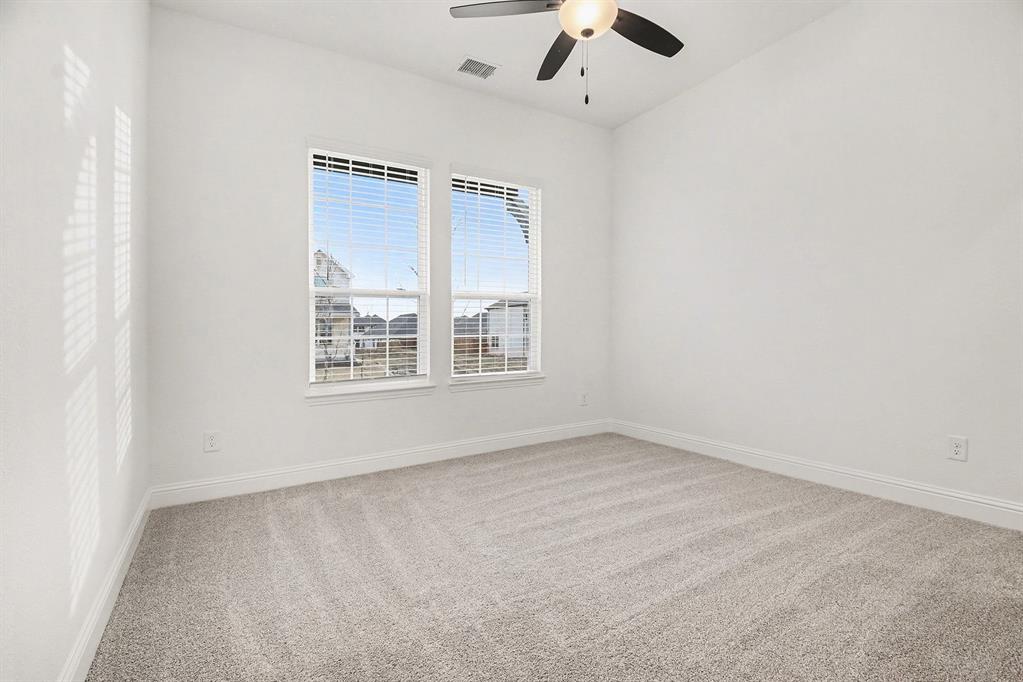 Interior space featuring neutral-toned carpeting, two windows with blinds, and a central ceiling fan with an integrated light fixture