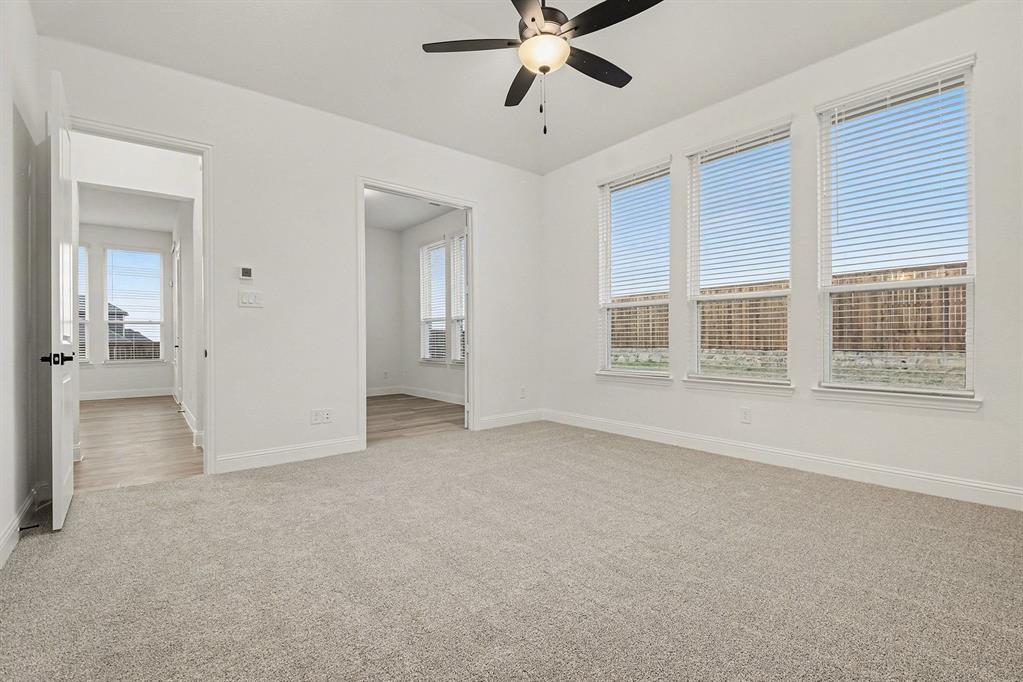 Neutral-toned carpeting, multi-pane windows with horizontal blinds, and a central ceiling fan with integrated lighting