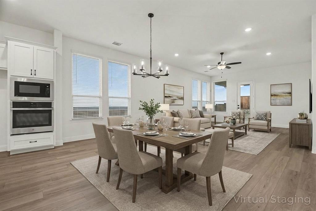 Open-concept interior featuring wood-finish flooring, recessed lighting, built-in stainless steel double wall ovens, a multi-arm chandelier, and multiple windows Open-concept interior featuring wood-finish flooring, recessed lighting, built-in stainless steel double wall ovens, a multi-arm chandelier, and multiple windows