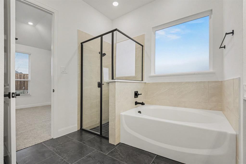 Soaking tub with a wall-mounted faucet, separate shower enclosure with a matte black frame, neutral-toned tiled surround, and dark floor tiling