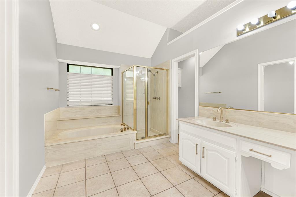 A deep soaking tub sits tucked under a bright window, surrounded by neutral tile and a separate glass shower. Unwind here after a busy week with a hot bubble bath and soothing candlelight.