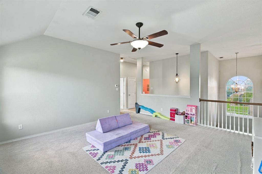Vaulted ceilings, neutral carpeting, a central ceiling fan with integrated lighting, a half-wall partition with pendant lighting, and an arched window with a wooden railing