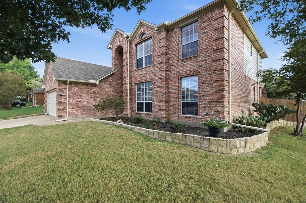 Two-story brick exterior featuring a multi-gabled roofline, grid-pattern windows, attached garage, and stone-bordered landscaping