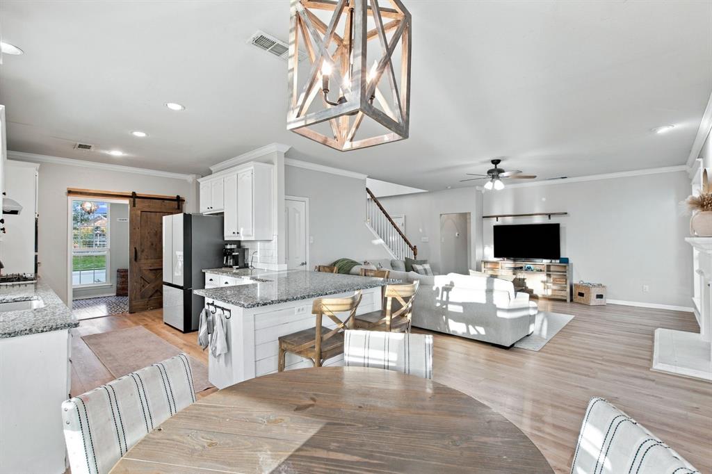 Open concept area featuring light wood-finish flooring, a kitchen island with stone countertops, a geometric chandelier, and a sliding barn door