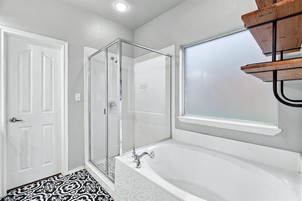 Bathroom featuring a glass-enclosed shower, a deep soaking tub, patterned floor tile, and built-in metal and wood-finish shelving