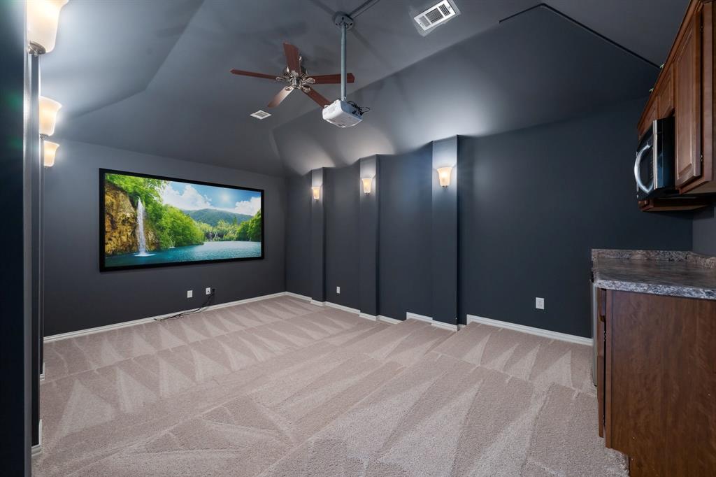 Dedicated media room featuring a large projection screen, recessed ceiling, and plush carpet flooring