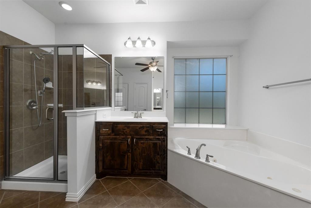 Corner soaking tub, separate glass-enclosed shower with tile surround, single vanity with dark wood-finish cabinetry, and tiled flooring