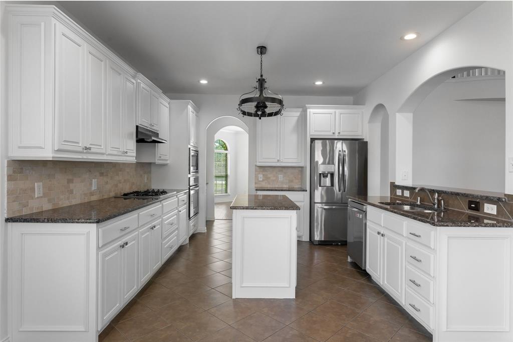 Kitchen with white cabinetry, dark stone countertops, stainless steel appliances, and a central island