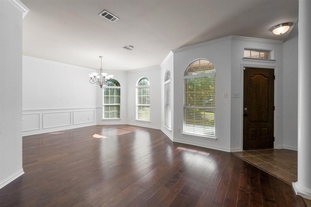 Dark wood-finish flooring, wainscoting detail, arched windows, and a classic chandelier