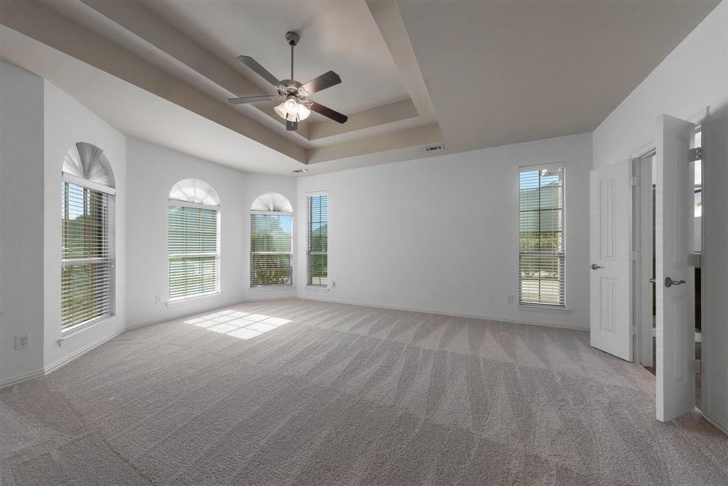 Spacious Master bedroom with tray ceiling, ceiling fan with light, multiple arched windows, and brand new carpet