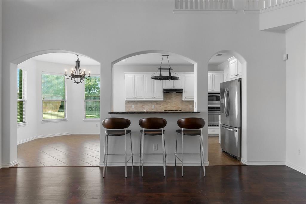 Arched doorways, dark wood-finish flooring, white kitchen cabinetry, stainless steel appliances, and a kitchen bar with a stone-finish countertop