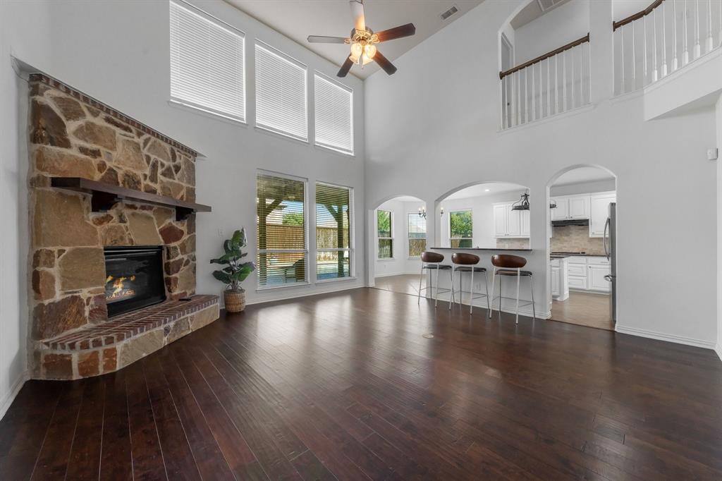 Vaulted ceilings with a ceiling fan, stone fireplace with a wood mantle, rich wood-finish flooring, and arched doorways
