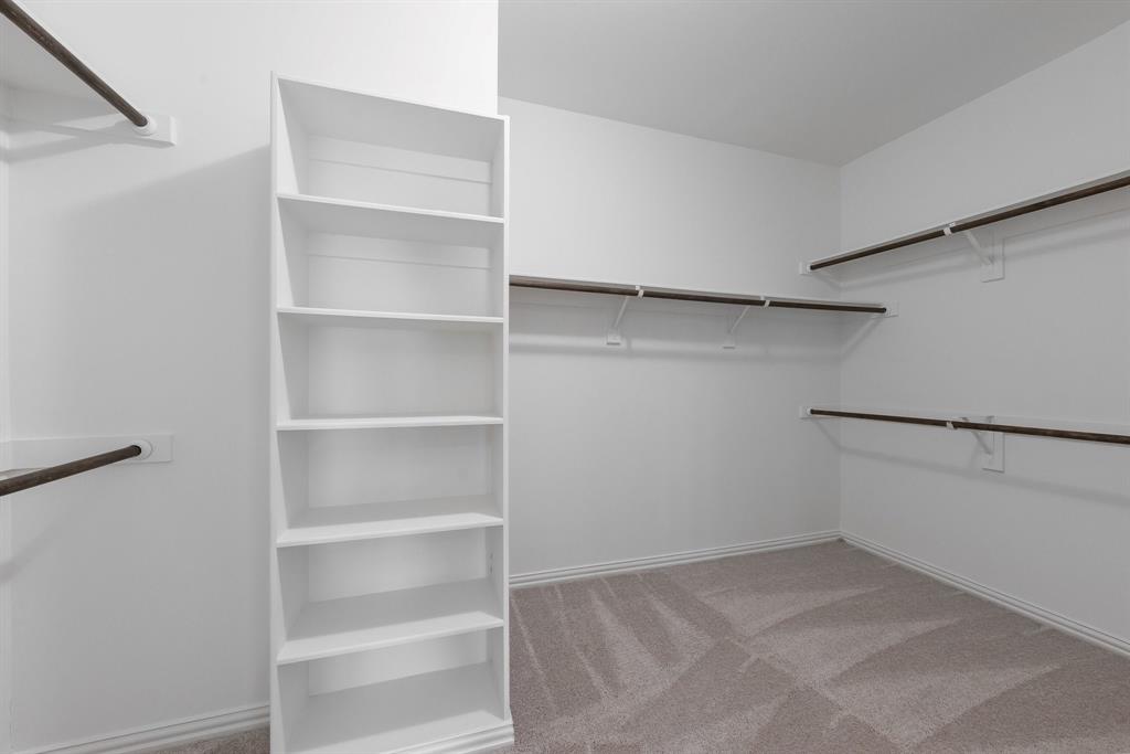 Built-in shelving unit, multiple clothing rods, light-toned carpeting, and painted walls