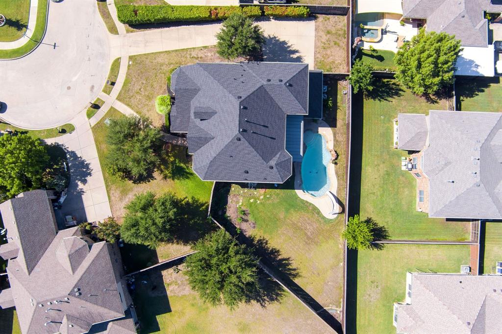 Expansive property featuring a curved swimming pool, dark shingle roof, and mature perimeter trees