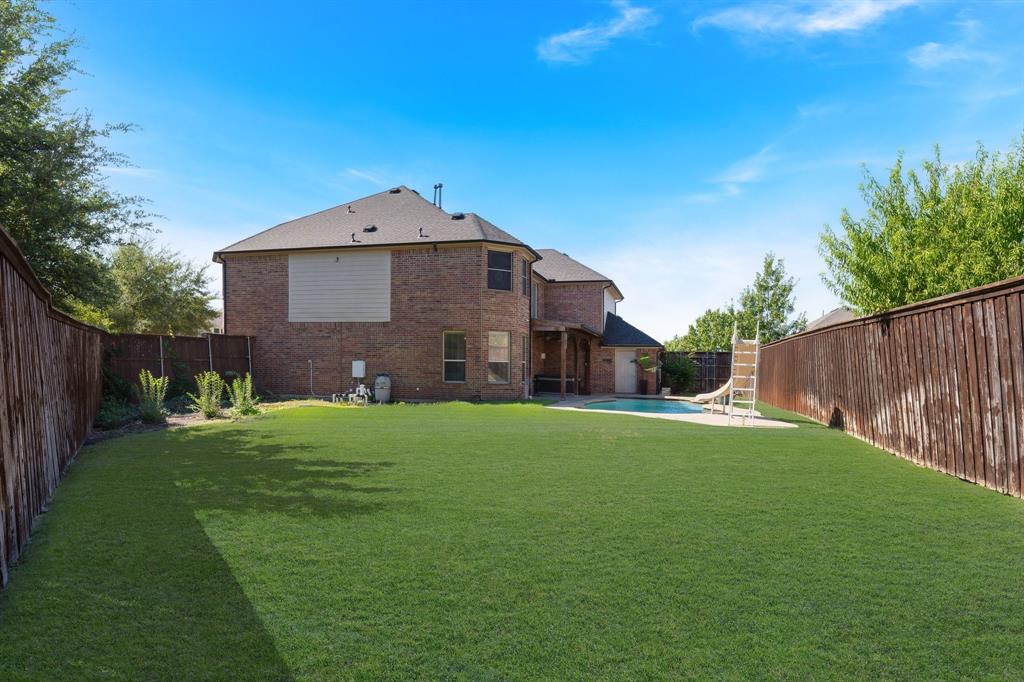 Expansive backyard featuring a manicured lawn, brick exterior, and a swimming pool