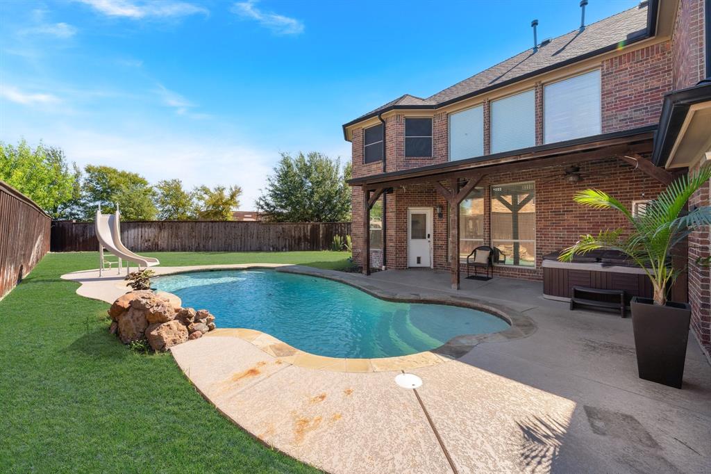 Brick exterior with a covered patio featuring a built-in spa, an in-ground swimming pool, and a fenced backyard with mature trees