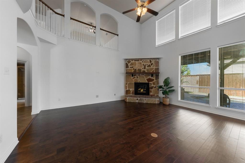 Vaulted ceiling with a ceiling fan, stone fireplace with a wood mantel, dark wood-finish flooring, and multiple large windows