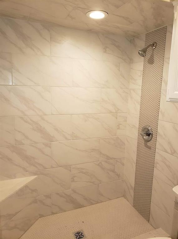 Tiled shower featuring rectangular wall tiles with subtle veining, a hexagon tile floor, a built-in corner bench, and a vertical hexagon tile accent strip