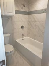 Bathroom featuring a white bathtub, toilet, and overhead cabinetry