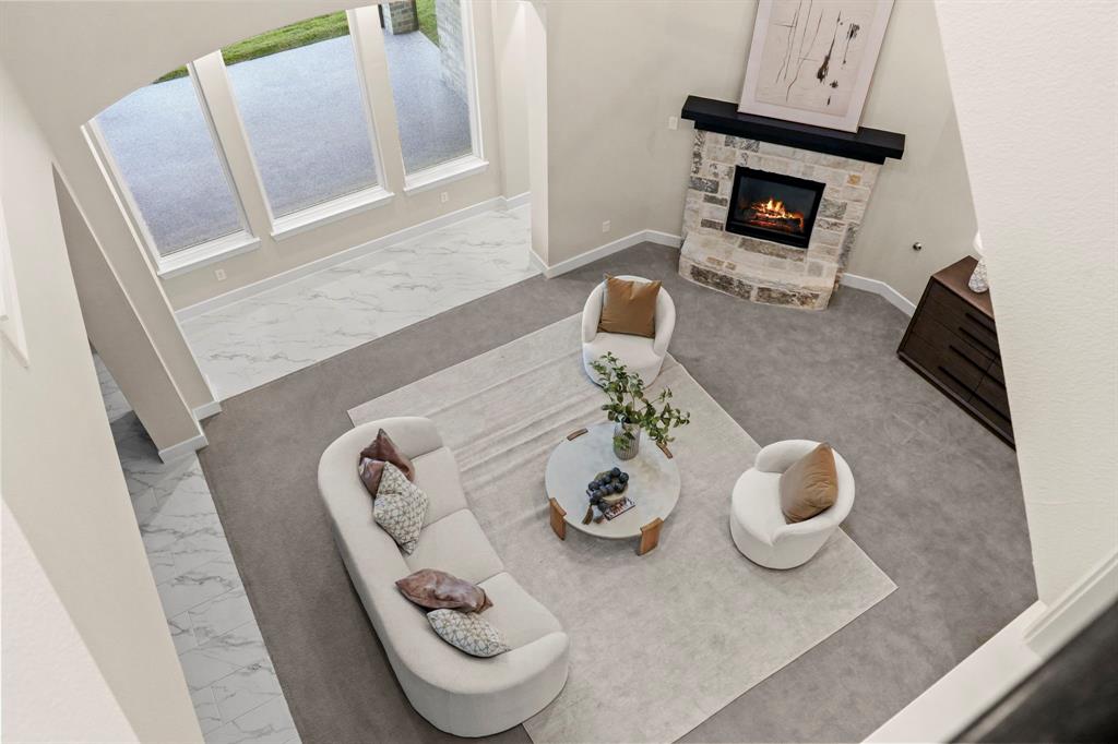 Two-story living area featuring floor-to-ceiling windows, natural stone fireplace with a floating mantle, and a combination of carpet and large-format tile flooring