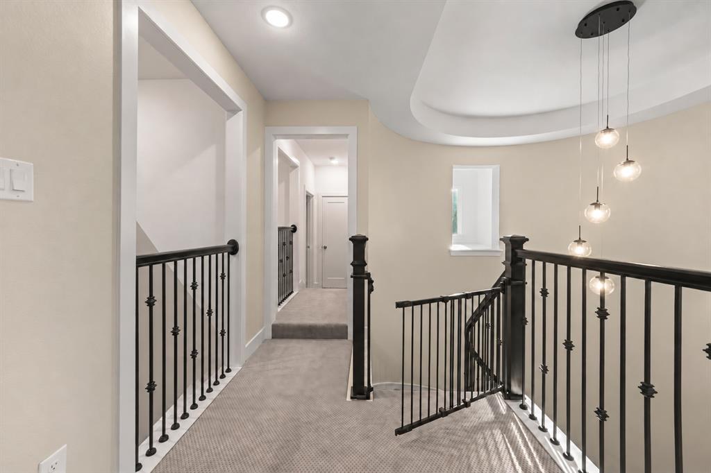 Neutral carpeting, wrought iron stair railing with ornate finials, tiered multi-globe pendant lighting, and recessed ceiling architecture