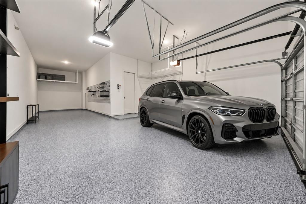 Spacious garage featuring high ceilings, epoxy-finished flooring, wall-mounted storage organization system, and overhead wire shelving