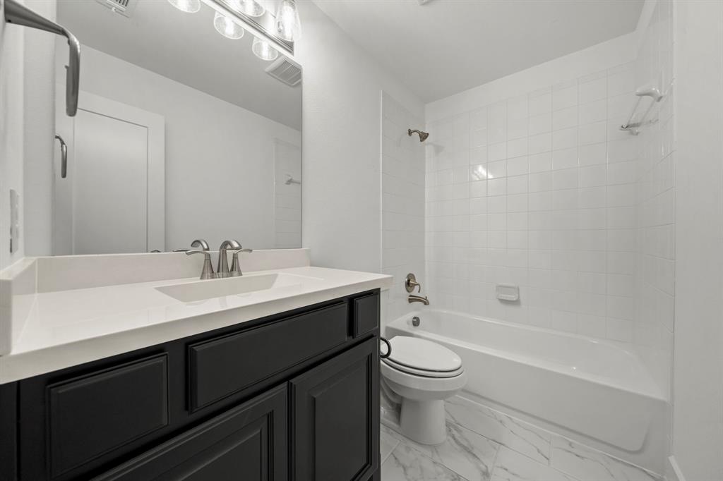 Dark-toned vanity with a solid-surface countertop, rectangular integrated sink, white tile shower surround, and patterned flooring
