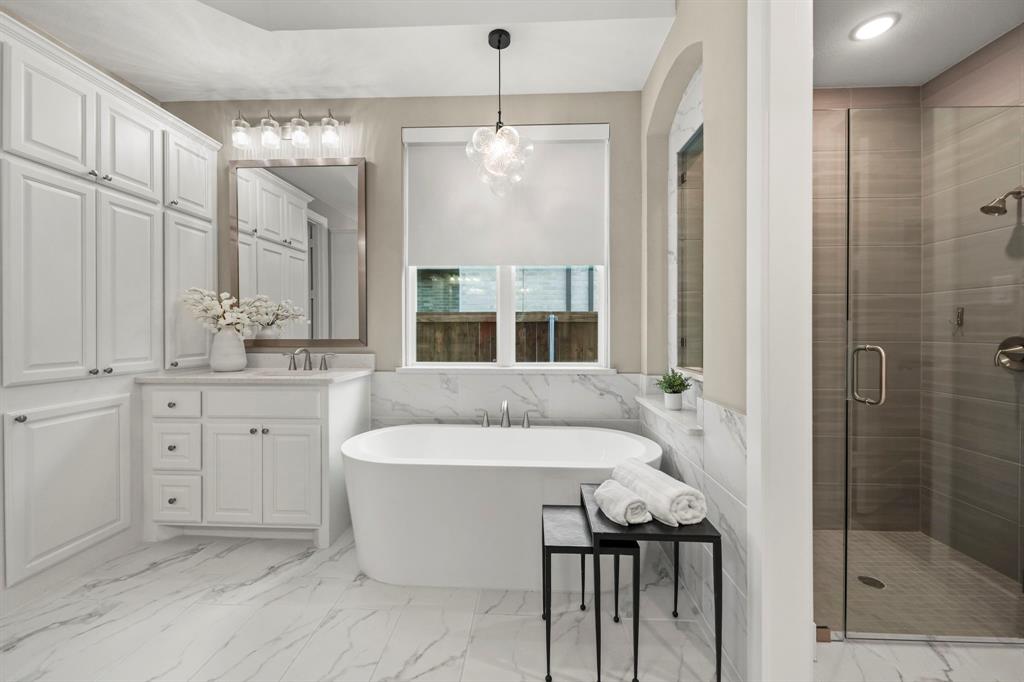 Freestanding soaking tub with stone-finish surround, white cabinetry, large-format tile flooring, and walk-in shower with glass enclosure