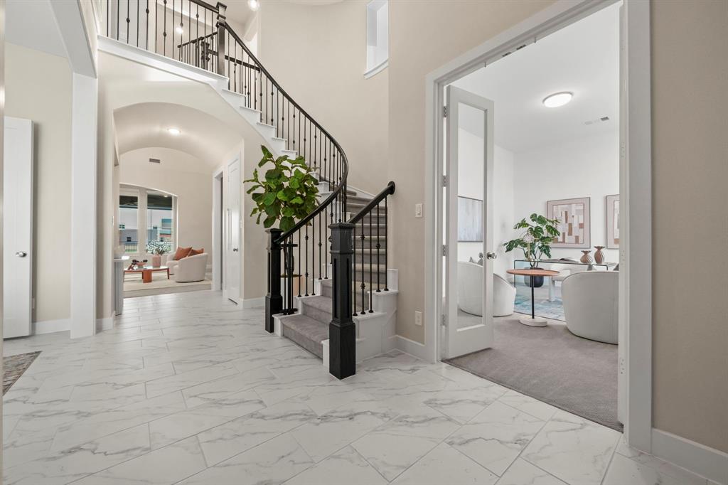 Grand foyer featuring large-format tile flooring, a curved staircase with wrought-iron balusters, an arched hallway, and a glass-paned French door entry to an auxiliary room