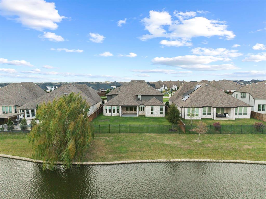Multi-gabled masonry exterior with a covered rear patio, positioned on a waterfront lot featuring a fenced backyard and a mature weeping willow