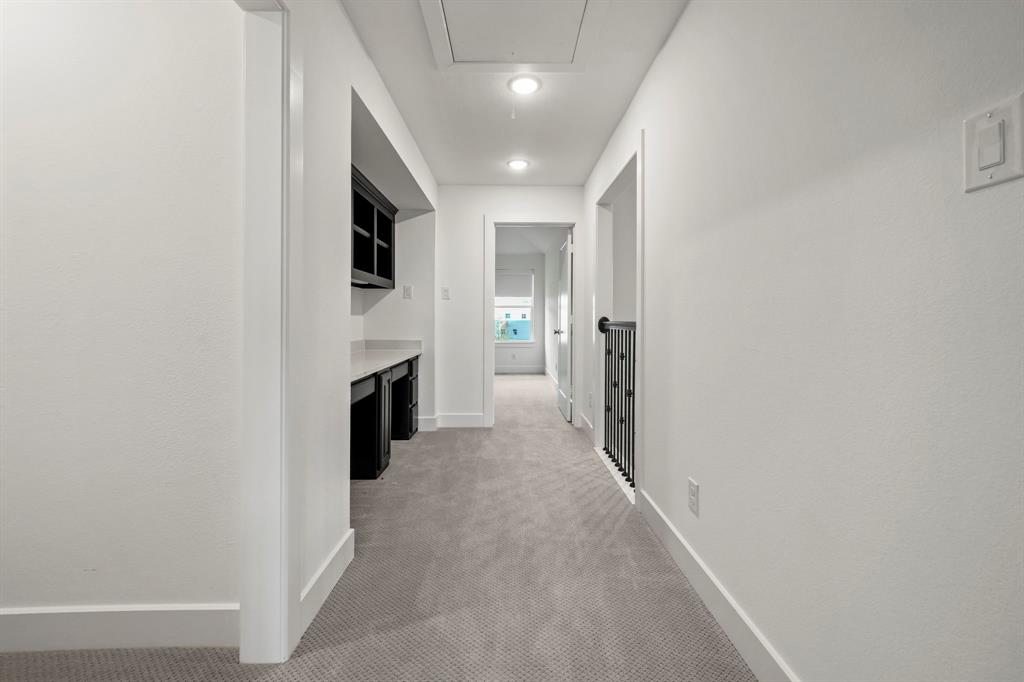 Hallway featuring wall-to-wall carpeting, built-in desk with dark cabinetry and stone-surface countertop, overhead recessed lighting, and metal stair railing