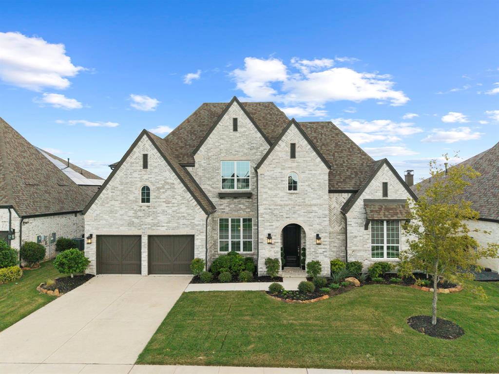 Stone and brick facade featuring multi-gabled rooflines, arched entryway, dark wood-finish garage doors, and manicured front landscaping