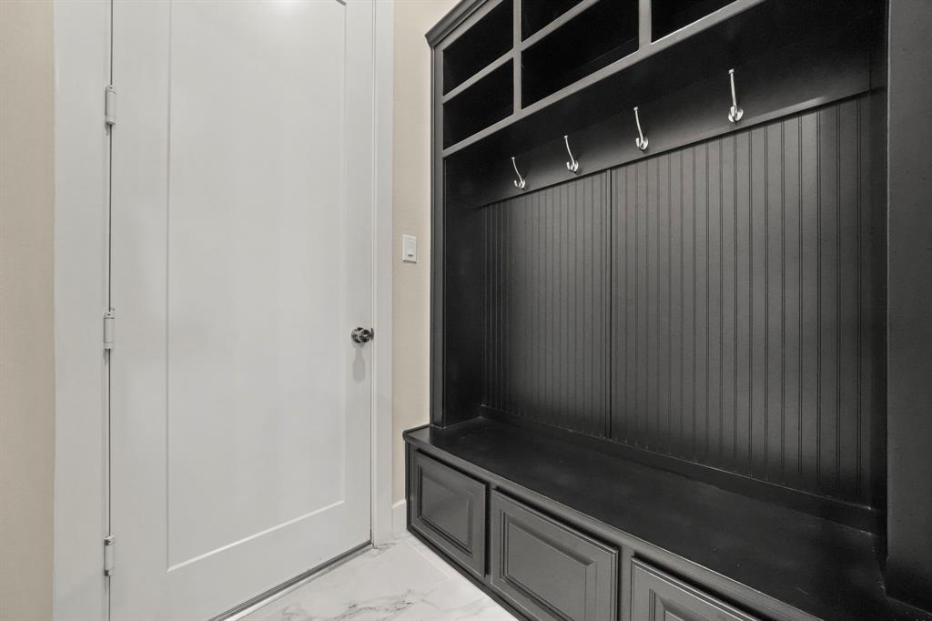 Built-in mudroom cabinetry featuring dark finish shaker-style lower drawers, beadboard paneling, integrated upper shelving, and metallic hooks, set against light-toned flooring