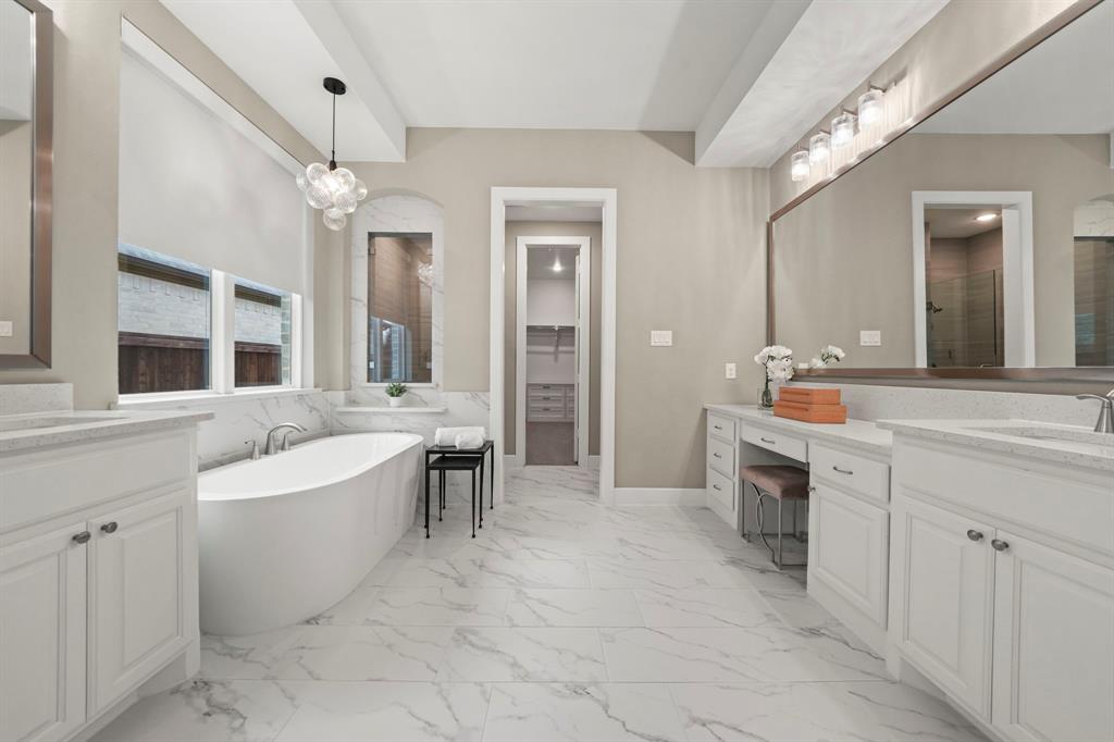 Bathroom featuring dual white vanities with stone-surface countertops, a freestanding soaking tub, large-format tile flooring, and a recessed vanity area