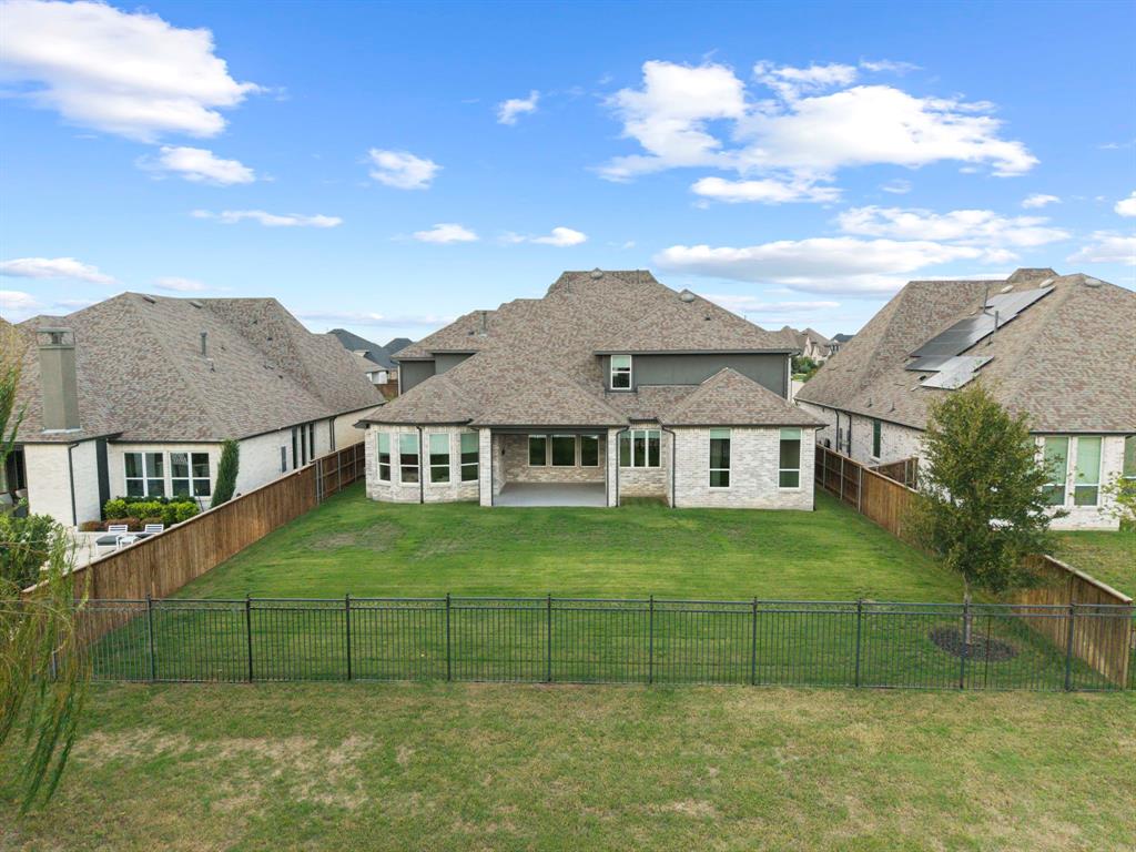 Rear exterior featuring light-toned masonry, a covered patio, multiple multi-pane windows, a fenced backyard, and a composition shingle roof