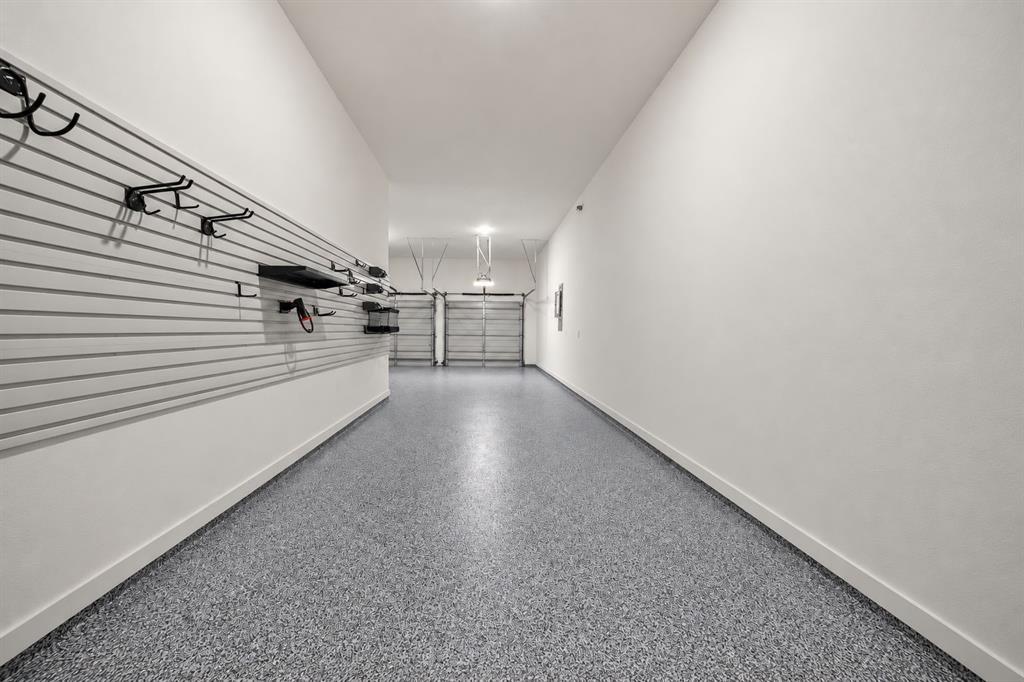 Garage featuring epoxy-coated flooring, heavy-duty wall-mounted slat wall storage system, and dual metal roll-up doors