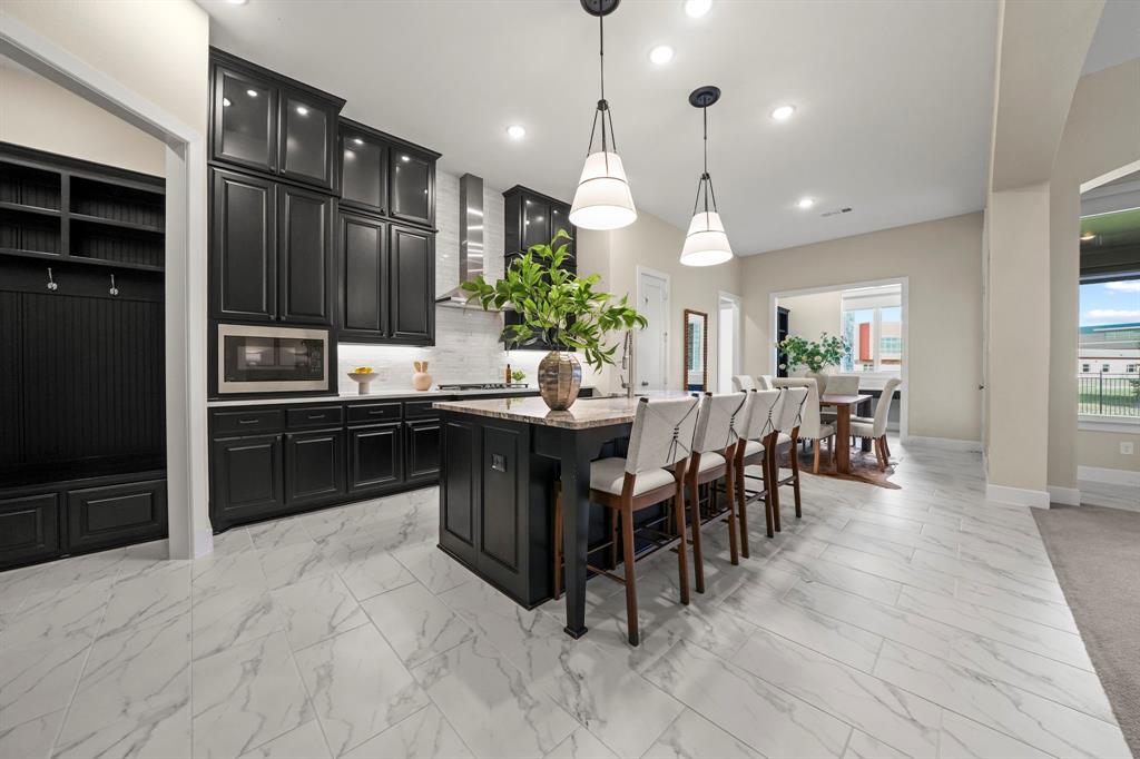 Kitchen featuring floor-to-ceiling dark cabinetry, stone-finish countertops, a central island, patterned tile flooring, and built-in mudroom storage