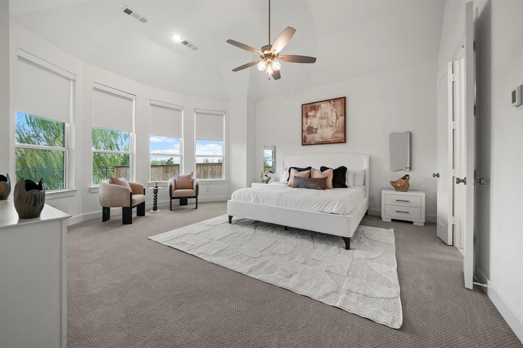 Vaulted ceiling, four-paneled bay window configuration, neutral carpeting, and a multi-blade ceiling fan with integrated lighting