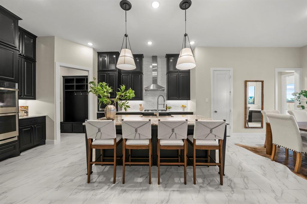 Kitchen featuring custom cabinetry, stone-surface central island, stainless steel double wall oven, metal range hood, and tile flooring