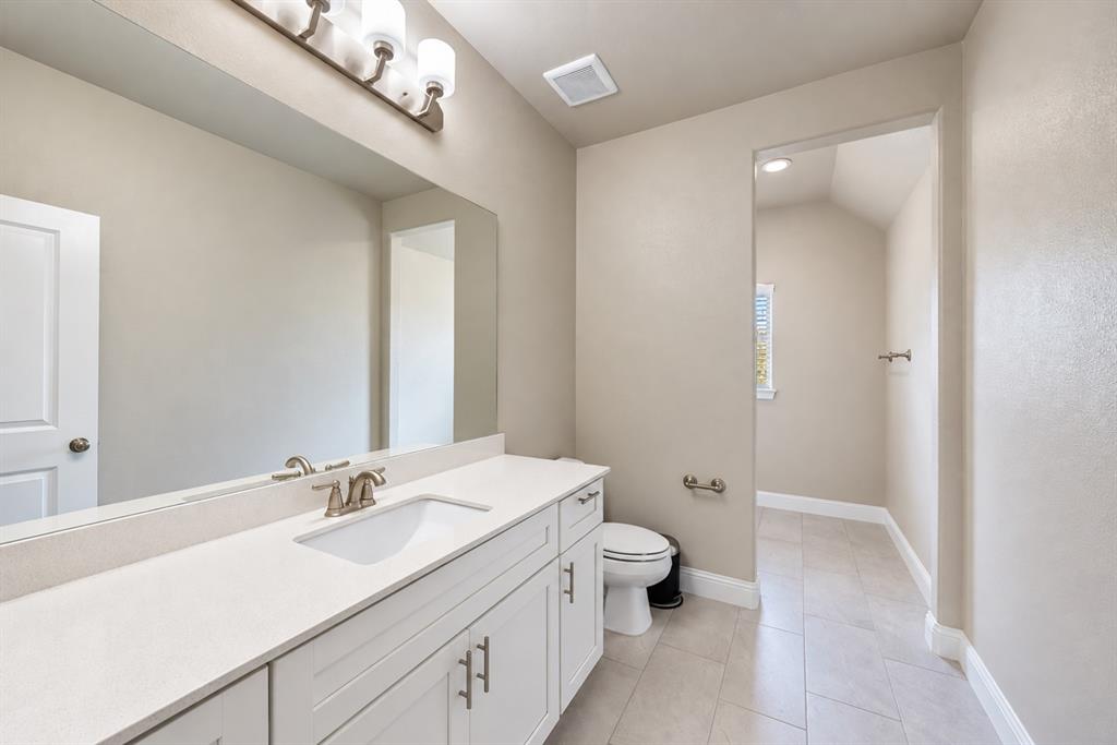White vanity with brushed nickel hardware, expansive vanity mirror, light-toned countertop, and recessed lighting