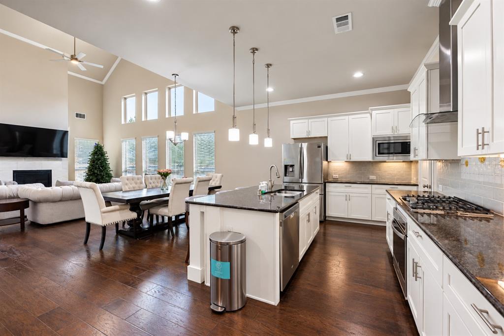 Spacious interior featuring soaring ceilings, wood-finish flooring, a contemporary fireplace, a kitchen island with pendant lighting, and stainless steel appliances