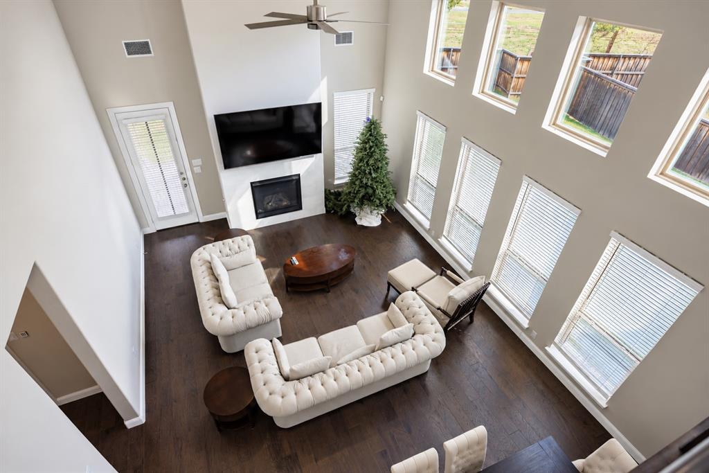 Soaring ceilings with a ceiling fan, multiple windows with blinds, a fireplace with a white surround, and dark wood-finish flooring