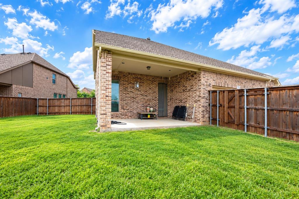 Expansive green lawn, brick exterior, covered patio, privacy fencing, and a window with dark trim